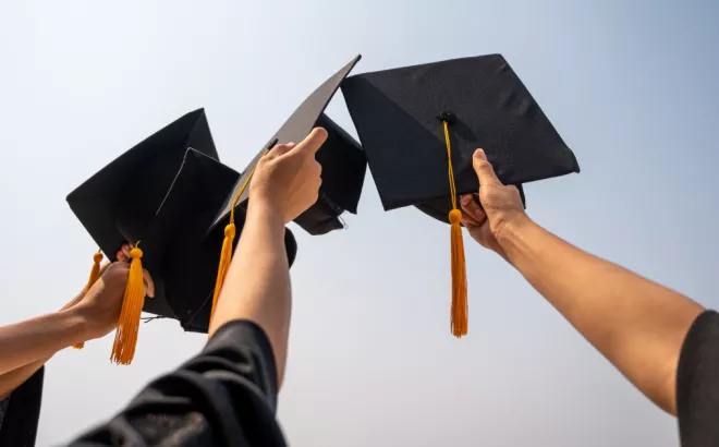 Drie afgestudeerde studenten die hun afstudeerhoeden omhoog houden