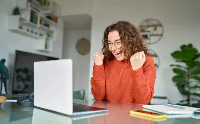 Une étudiante qui se réjouit après avoir créé un bon CV sur son ordinateur.