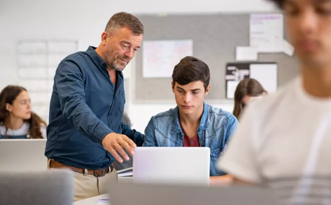 Un professeur montre quelque chose à un de ses étudiants sur son ordinateur portable